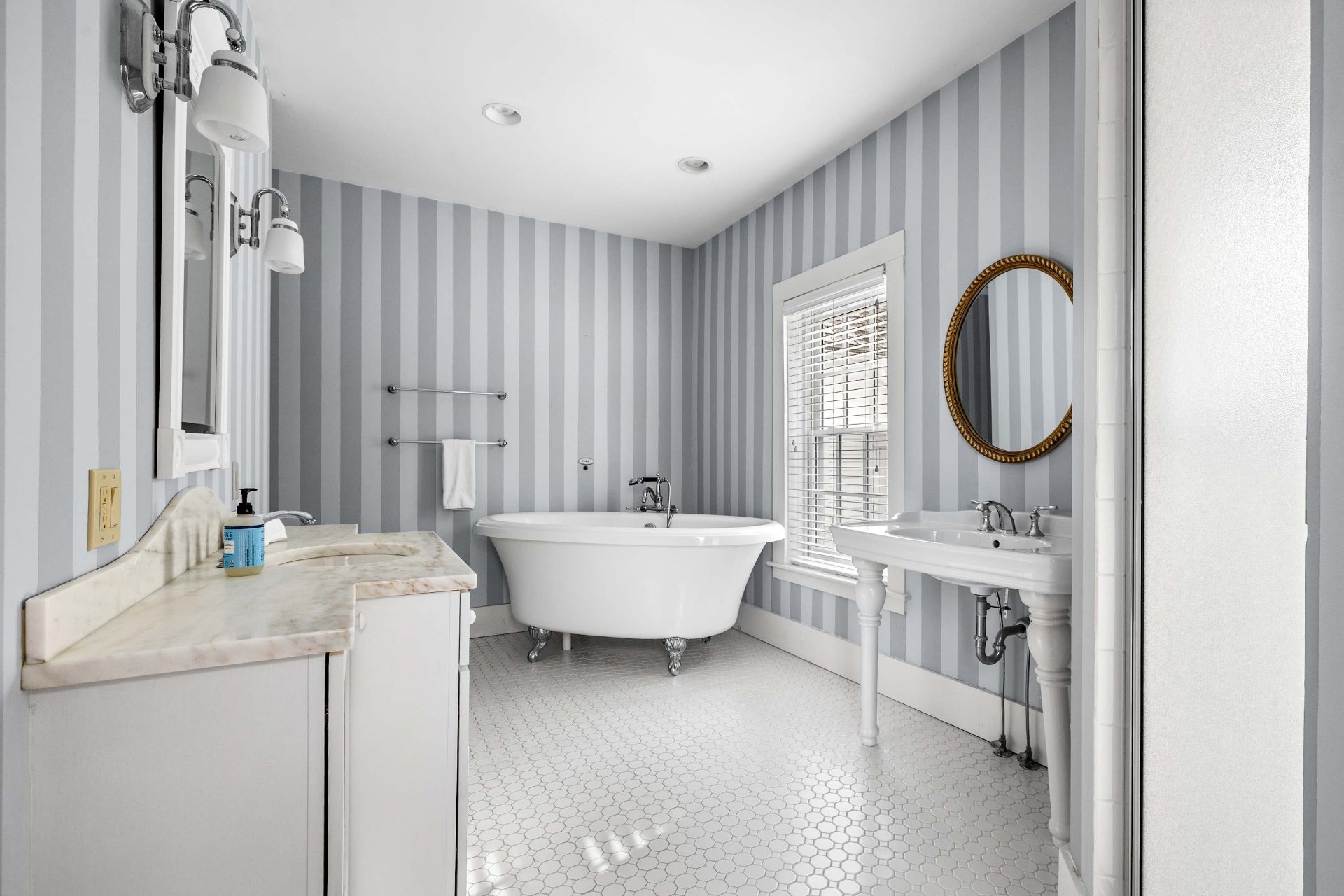 Primary bathroom with clawfoot soaking tub, marble vanity, and striped wallpaper