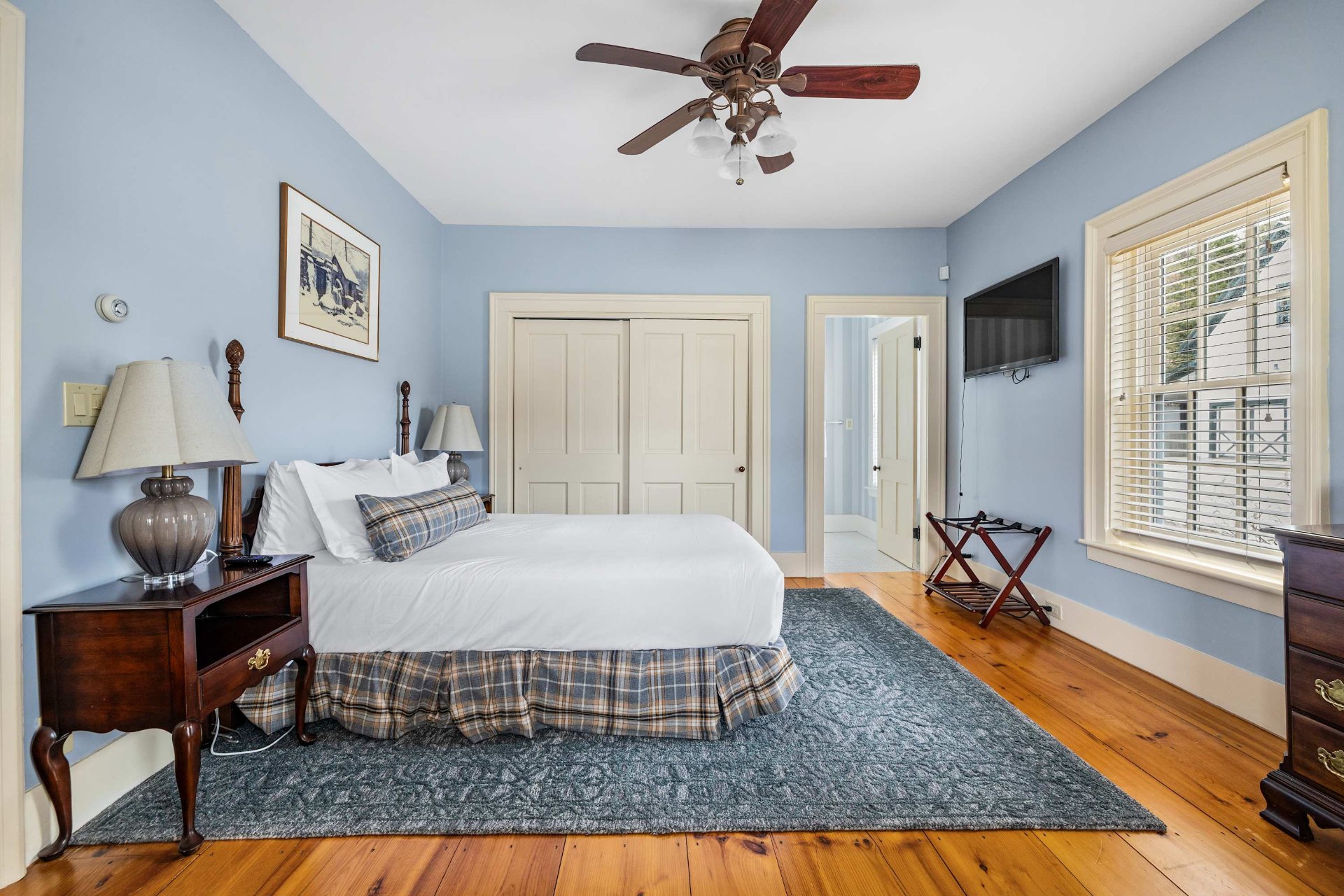 Primary bedroom with four-poster king bed, wide-plank pine floors, and bay window